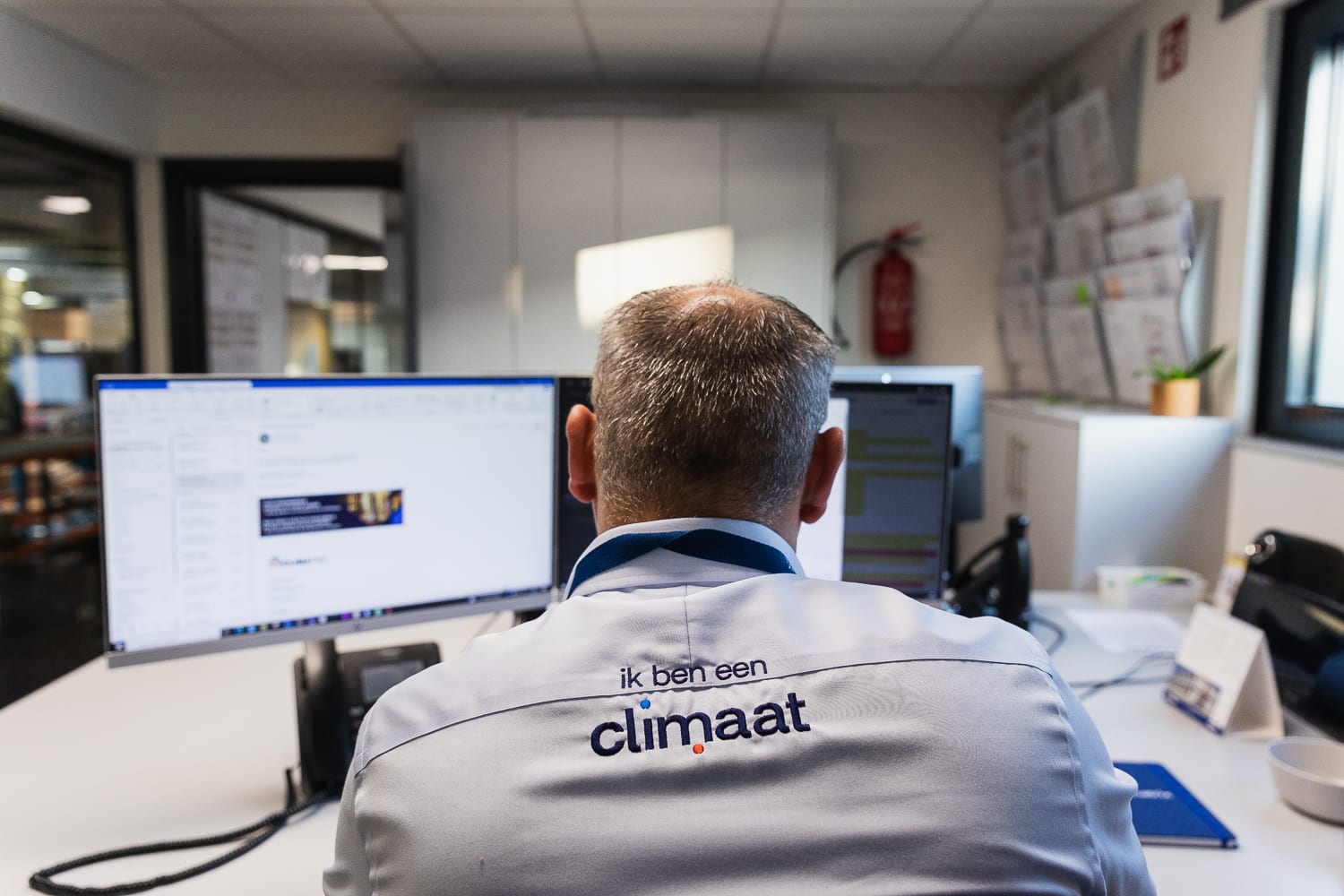Een medewerker van Climatrix zit achter zijn computer. Hij draagt een hemd met op de achterkant 